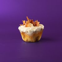 A cinnamon roll cupcake with bacon baked in, topped with vanilla buttercream, and finished with a cinnamon roll glaze drizzle, cinnamon sugar sprinkles, and bacon pieces. Bacon Cinnamon Roll cupcake
