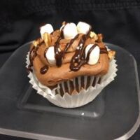A chocolate cupcake with pecans, filled with marshmallow fluff, topped with chocolate butter cream, and finished with chopped mini marshmallows, chopped pecans and a chocolate ganache drizzle. Mississippi Mud