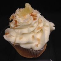 A pineapple cupcake filled with coconut pudding, topped with cream cheese icing and finished with toasted coconut and a dried pineapple tidbit. Piña Colada