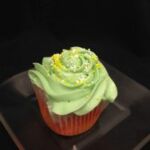A watermelon cupcake topped with green watermelon cream cheese and finished with yellow and white jimmies. Watermelon