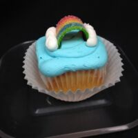 A vanilla cupcake with a skittles candy filling, topped with blue vanilla buttercream, and finished with vanilla butter cream clouds and a rainbow candy piece. End of the Rainbow