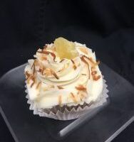 A pineapple cupcake filled with coconut pudding, topped with cream cheese frosting and finished with toasted coconut shavings and a dried pineapple tidbit. Pina Colada