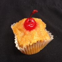 A pineapple cupcake topped and filled with pineapple upside down cake topping and finished with a cherry. Pineapple Upside Down