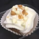 A white chocolate cupcake with chopped macadamia nuts baked in, topped with a vanilla buttercream and finished with white chocolate chips and finely chopped macadamia nuts. White Chocolate Macadamia Nut