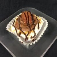 A chocolate cupcake with a caramel pecan filling, topped with caramel and chocolate buttercream, and finished with chocolate and caramel drizzle and a full toasted pecan. Turtle
