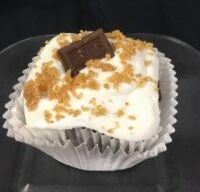 A chocolate cupcake filled with a marshmallow graham cracker mixture, topped with marshmallow buttercream and finished with a 1/4 Hershey's chocolate piece and graham cracker crumbs. S'Mores