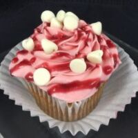 A white chocolate raspberry cupcake topped with raspberry cream cheese and finished with a raspberry jam drizzle and white chips. White Chocolate Raspberry