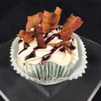 A blueberry maple bacon cupcake, filled with a blueberry bacon mixture, frosted with maple buttercream then topped with bacon strips and blueberry drizzle. Blueberry Maple Bacon