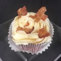 A red velvet cupcake with a crumbled bacon and maple syrup mixture for the filing, topped with cream cheese frosting, cut bacon and a maple syrup drizzle. Christmas Morning