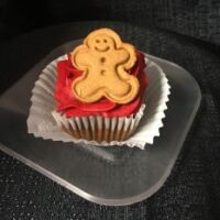 A gingerbread cupcake topped with red gingerbread cream cheese frosting and finished with a mini gingerbread man cookie. Gingerbread