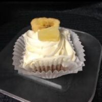 A banana, pineapple and pecan cupcake topped with cream cheese icing and finished with a banana chip and a dried pineapple tidbit. Hummingbird