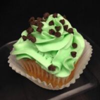 A white cupcake with chocolate chips and mint flavoring, topped with green mint cream cheese icing and finished with mini chocolate chips. Mint Chocolate Chip