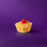 A pineapple cupcake topped and filled with pineapple upside down cake topping and finished with a cherry. Pineapple Upside Down cupcake