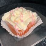 A strawberry cupcake with a white ganache filling, cream cheese icing, strawberry ganache drizzle, and topped with white morsels. White Chocolate Strawberry