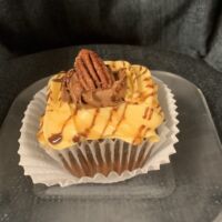 A chocolate cupcake with a caramel pecan filling, topped with caramel and chocolate buttercream icings, and finished with chocolate and caramel drizzles and a full toasted pecan. Turtle Cupcake