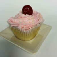 A vanilla cupcake with a cherry ganache filling, cherry cream cheese icing, white ganache drizzle, and a cherry on top. White Chocolate Cherry